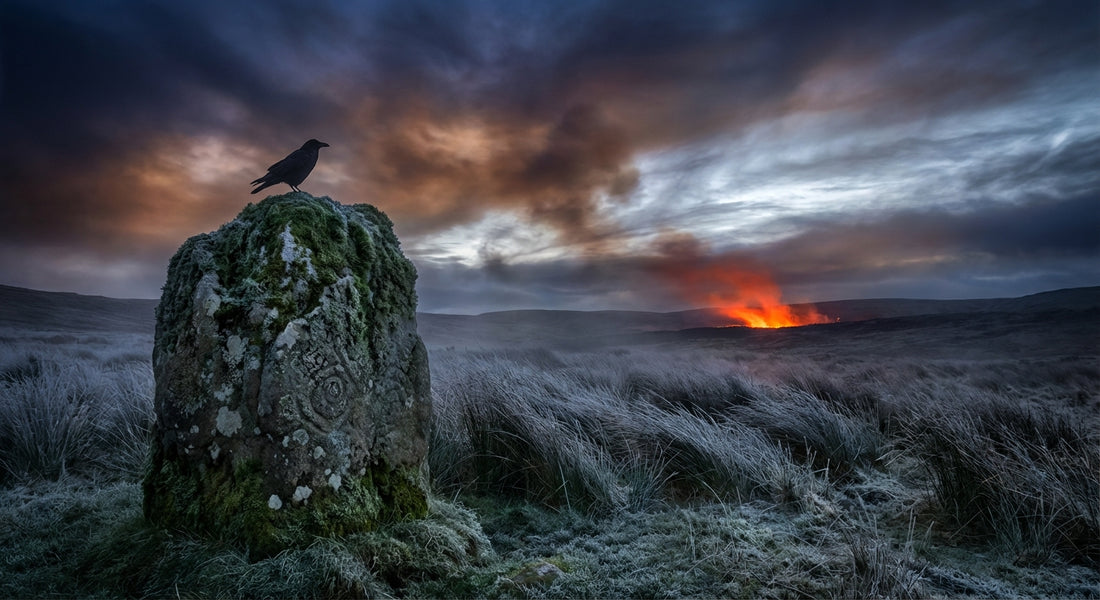 A raven perches on a moss-covered standing stone at twilight, surrounded by frost-touched grasses and a smoldering amber glow on the horizon, evoking the threshold between worlds in a wild Celtic landscape.