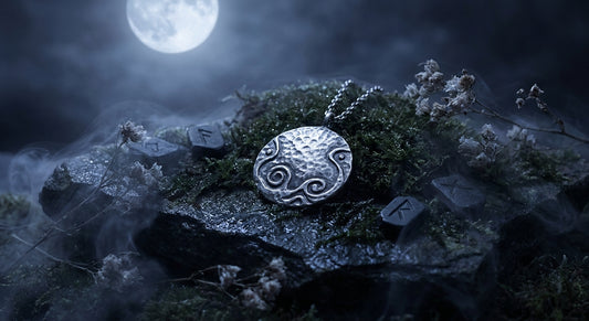 A silver talisman pendant resting on a mossy stone beneath a glowing full moon, surrounded by mist and dried wildflowers in a mystical nighttime setting.
