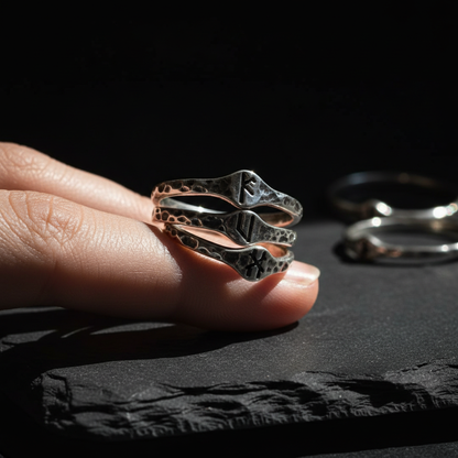Signet rune band rings stacked on a finger, oxidized sterling silver with 3mm Elder Futhark rune stamps, organic pitted texture, dark moody product photography